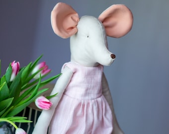 May include: A white plush mouse wearing a pink and white striped dress sits on a white suitcase with a star pattern. The mouse has large pink ears and a brown nose.