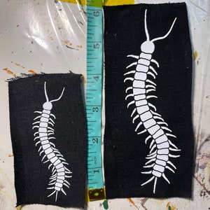 May include: Two black fabric patches with white outlines of a centipede. The larger patch is about 6 inches tall and the smaller patch is about 3 inches tall.