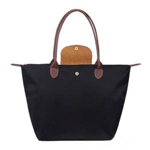 May include: Black tote bag with brown leather handles and trim. The bag has a rectangular shape with a zippered top and a snap closure. A small, tan-colored pouch is visible inside the bag.