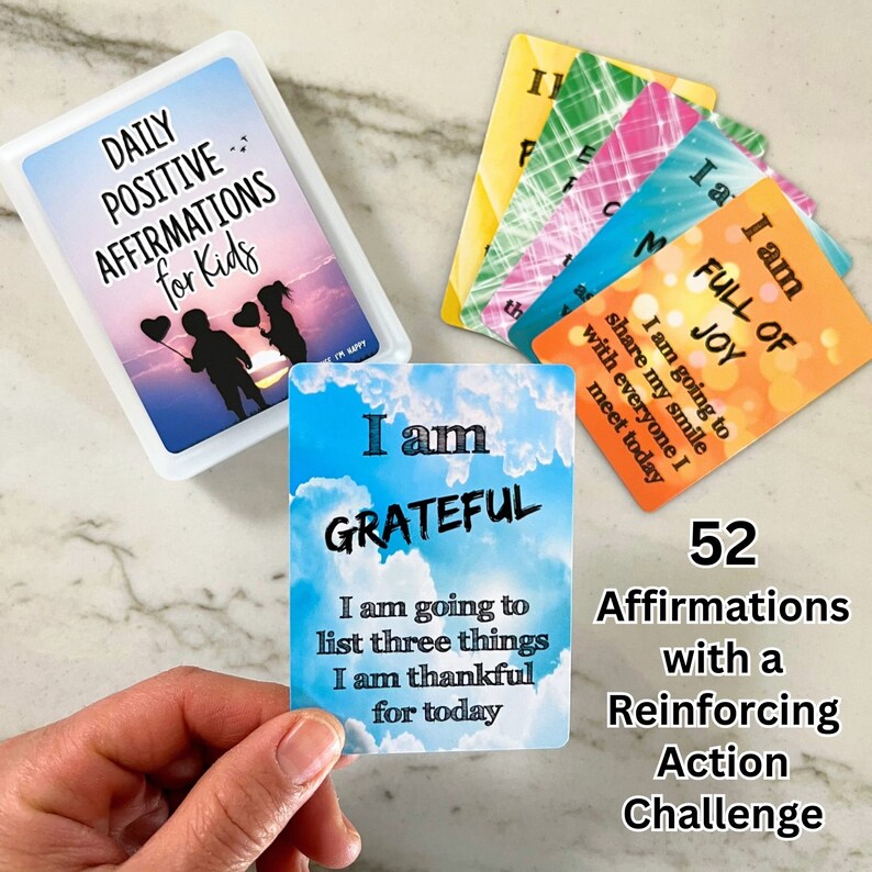 K&ouml;nnte beinhalten: Ein Set mit 52 Affirmationskarten mit blauem Himmel und Wolken als Hintergrund. Die Karten zeigen positive Affirmationen f&uuml;r Kinder. Der Text auf der gezeigten Karte lautet: "Ich bin dankbar. Ich werde drei Dinge auflisten, f&uuml;r die ich heute dankbar bin."