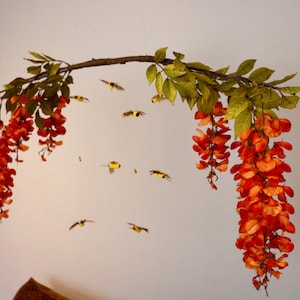 May include: A decorative branch with orange flowers hanging from it. The branch is suspended from the ceiling and has small yellow birds flying around it.
