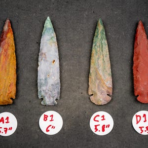 May include: Four colorful, hand-crafted arrowheads with varying hues of red, yellow, green, and white. Each arrowhead is labeled with a letter and measurement in inches, ranging from 5.5" to 6".