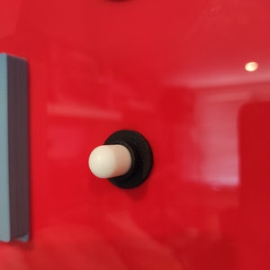 May include: Close-up of a red surface with a white button and a black ring. A pink button is visible at the top. A light blue rectangular object is on the left side.