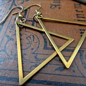 May include: A pair of gold triangle earrings with a geometric design. The earrings are made of brass and have a simple, modern style.