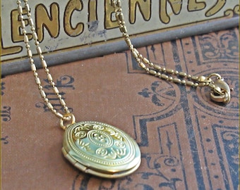 May include: A gold locket necklace with a detailed engraved design on the front. The necklace is on a chain with a lobster clasp.