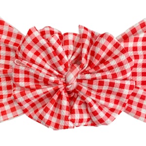 May include: A red and white gingham bow headband. The bow is tied in a knot and has a ruffled texture.