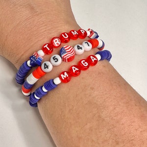May include: Three beaded bracelets with red, white, and blue beads. The top bracelet spells "TRUMP" in red letters. The middle bracelet has a small American flag bead and the numbers "45" in white letters. The bottom bracelet spells "MAGA" in red letters.