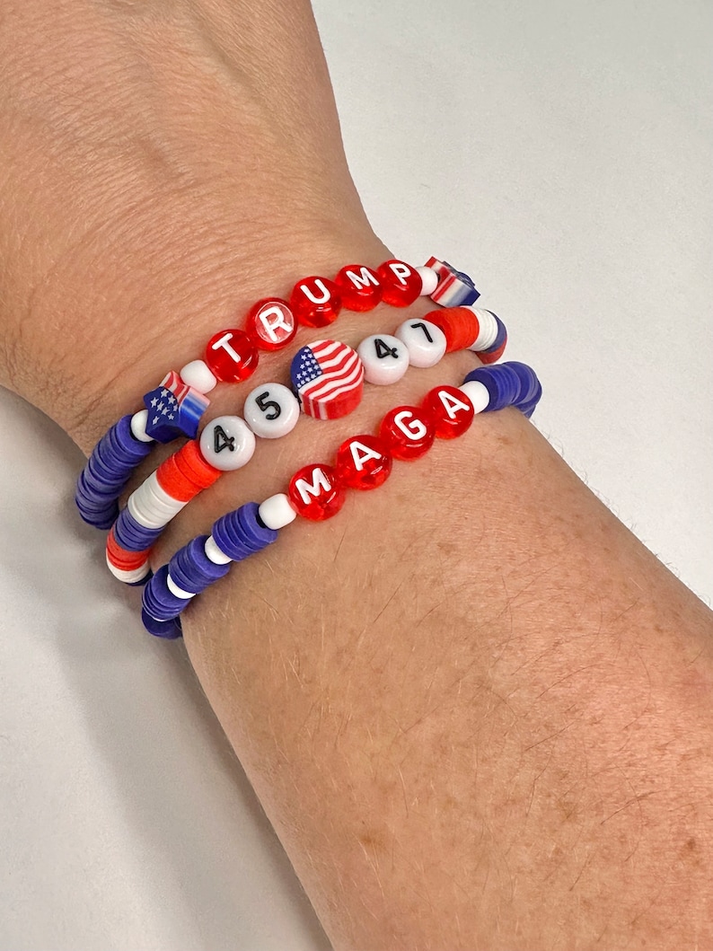 May include: Three beaded bracelets with red, white, and blue beads. The top bracelet spells "TRUMP" in red letters. The middle bracelet has a small American flag bead and the numbers "45" in white letters. The bottom bracelet spells "MAGA" in red letters.