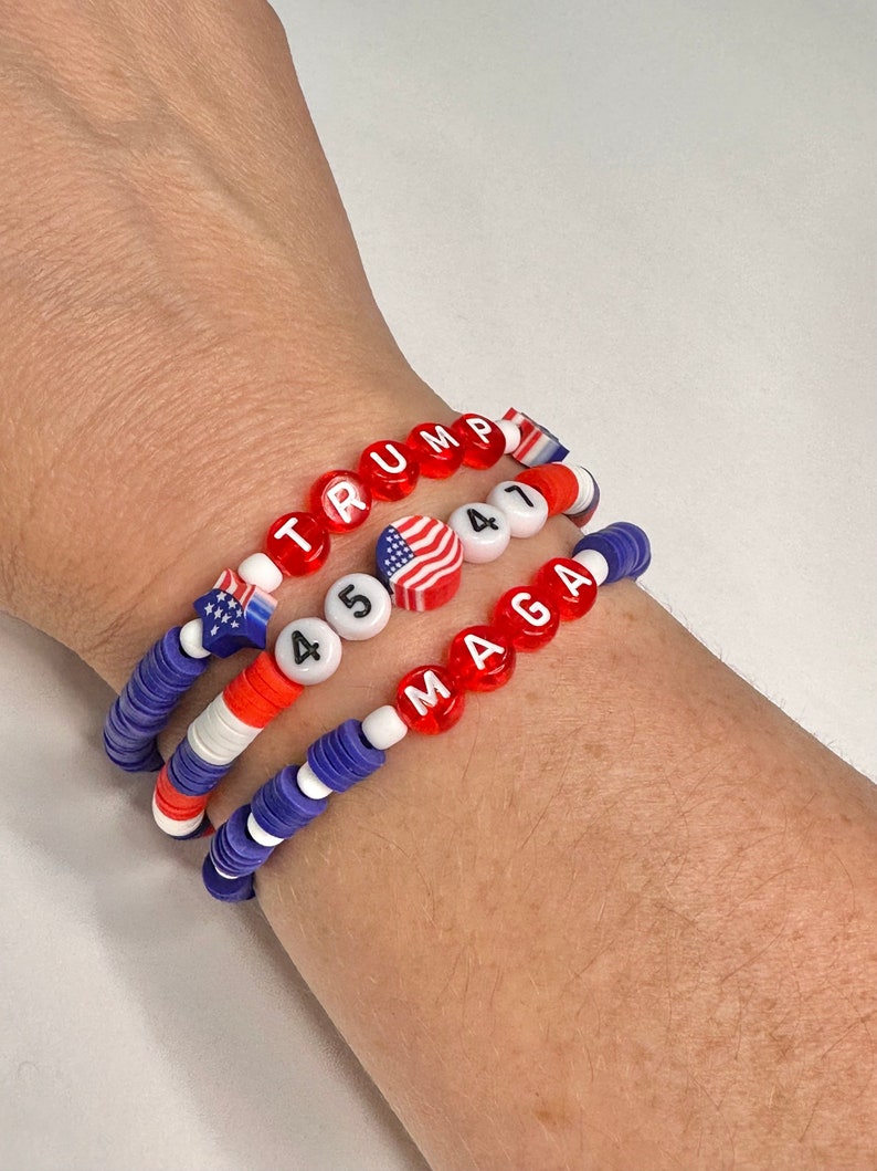 May include: Three beaded bracelets with red, white, and blue beads. The top bracelet spells "TRUMP" in red beads. The middle bracelet has white beads with the numbers "45" and a small American flag bead. The bottom bracelet spells "MAGA" in red beads.
