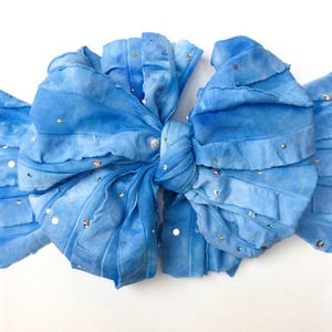 May include: A blue fabric bow with a ruffled texture and scattered iridescent sequins.