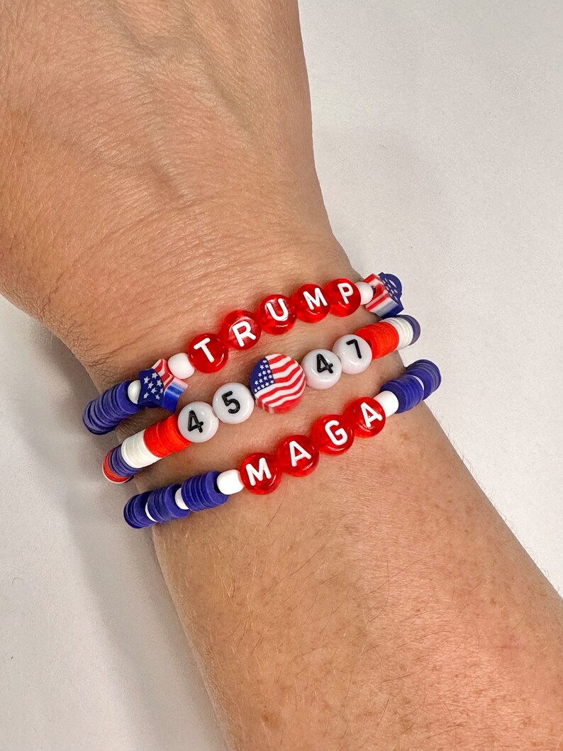 May include: Three beaded bracelets with red, white, and blue beads. The top bracelet spells out "TRUMP" in red beads. The middle bracelet has two American flag beads and the numbers "45" and "47" in white beads. The bottom bracelet spells out "MAGA" in red beads.
