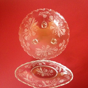 May include: Two clear glass serving dishes with a floral pattern. The larger dish has a scalloped edge and three feet. The smaller dish is oval shaped.