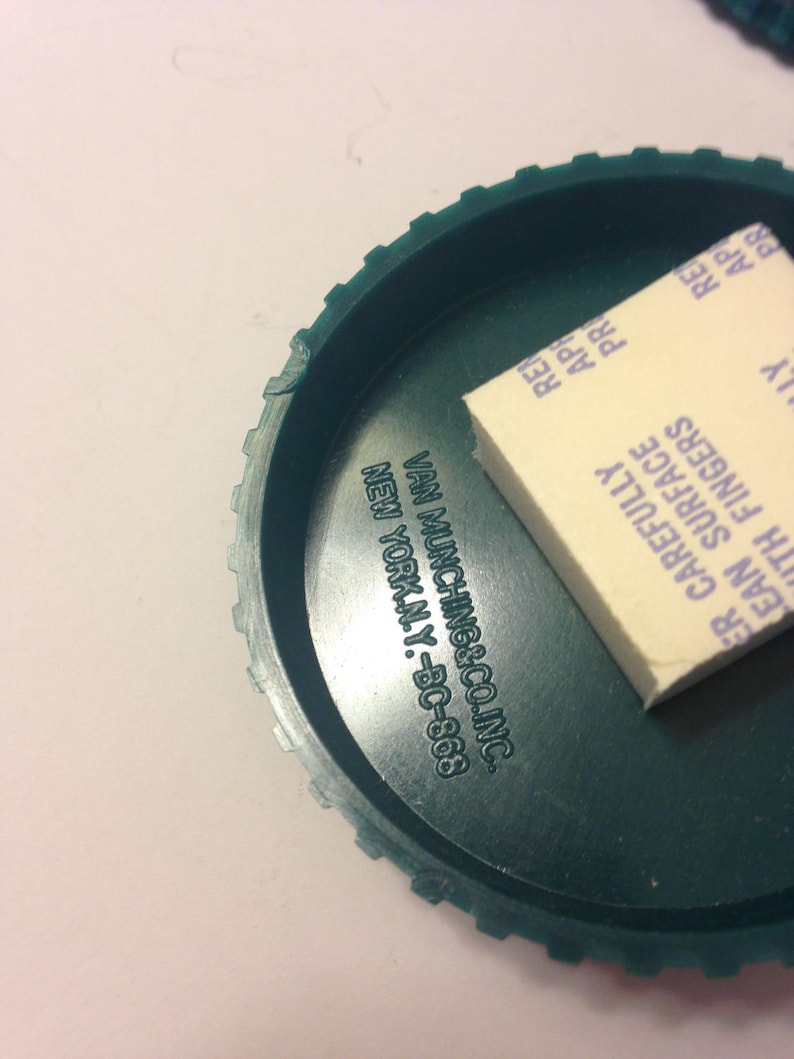 May include: A green plastic lid with a white adhesive sticker. The sticker has the text "Clean Surface Carefully With Fingers" and "Van Munching & Co. Inc. New York, N.Y. - BC-868".