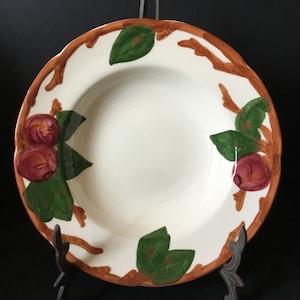 May include: A white ceramic soup bowl with a brown and green floral design. The bowl features a repeating pattern of brown branches, green leaves, and red apples.