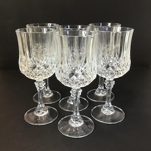 May include: Set of six clear glass wine glasses with a diamond-cut pattern. The glasses have a tall, slender stem and a wide bowl.
