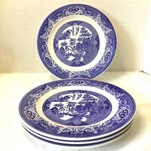 May include: A set of four white and blue Willow pattern plates. The plates feature a central landscape scene with pagodas, birds, and a decorative border. The plates are stacked, with one plate displayed separately.
