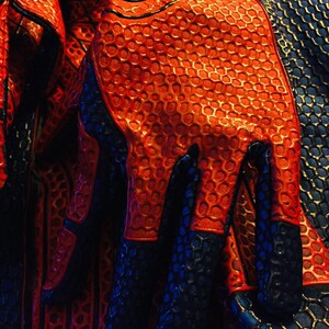 May include: Close-up of a red and blue fabric with a honeycomb pattern. The fabric is textured and has a glossy finish.