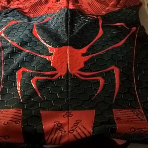 May include: Black and red spandex fabric with a spider design. The spider is red and has a black honeycomb pattern on its body.