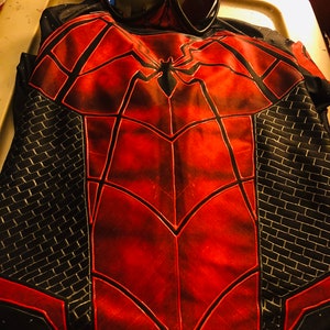 以下が含まれることがあります： 胸に黒いクモのシンボルが付いた赤と黒のスパイダーマンのコスチューム。コスチュームは側面に黒いメッシュのデザインと、赤いクモのデザインが施された黒いマスクが付いています。