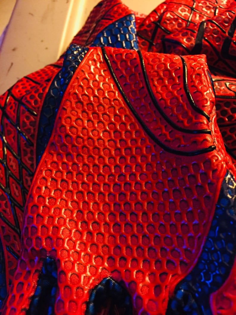 May include: Close-up of a red and blue fabric with a textured pattern. The fabric has a honeycomb-like design with black lines.