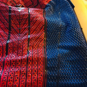 May include: Red and blue fabric with a spider web pattern and a honeycomb pattern. The fabric is folded in half.