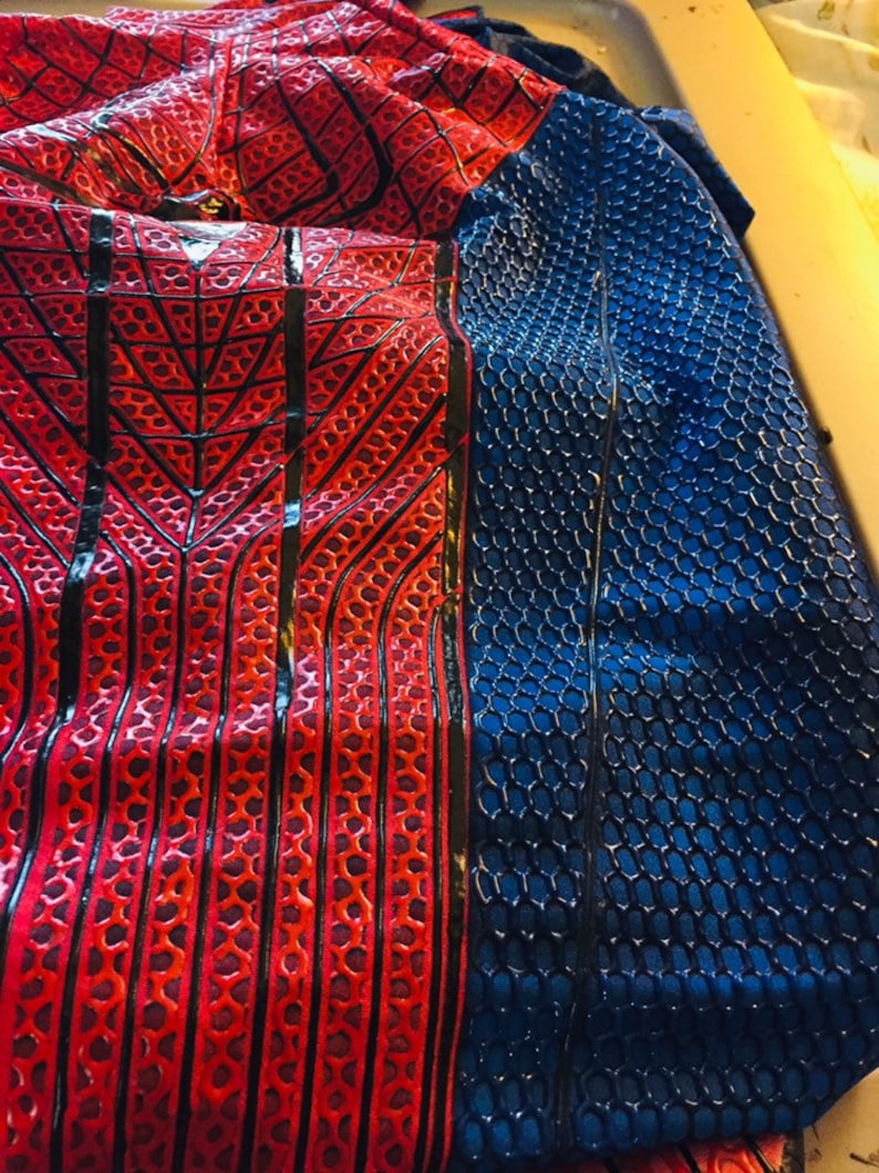 May include: Red and blue fabric with a spider web pattern and a honeycomb pattern. The fabric is folded in half.