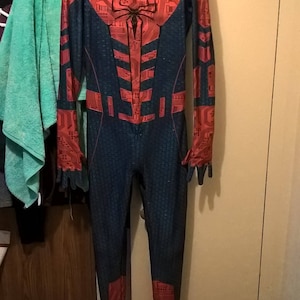 May include: A red and black Spiderman costume with a circuit board design. The costume has a hood and a mask with white eyes.