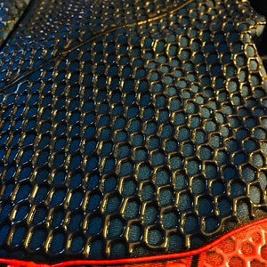 May include: Close-up of a black and red fabric with a honeycomb pattern. The fabric has a shiny, almost wet look.