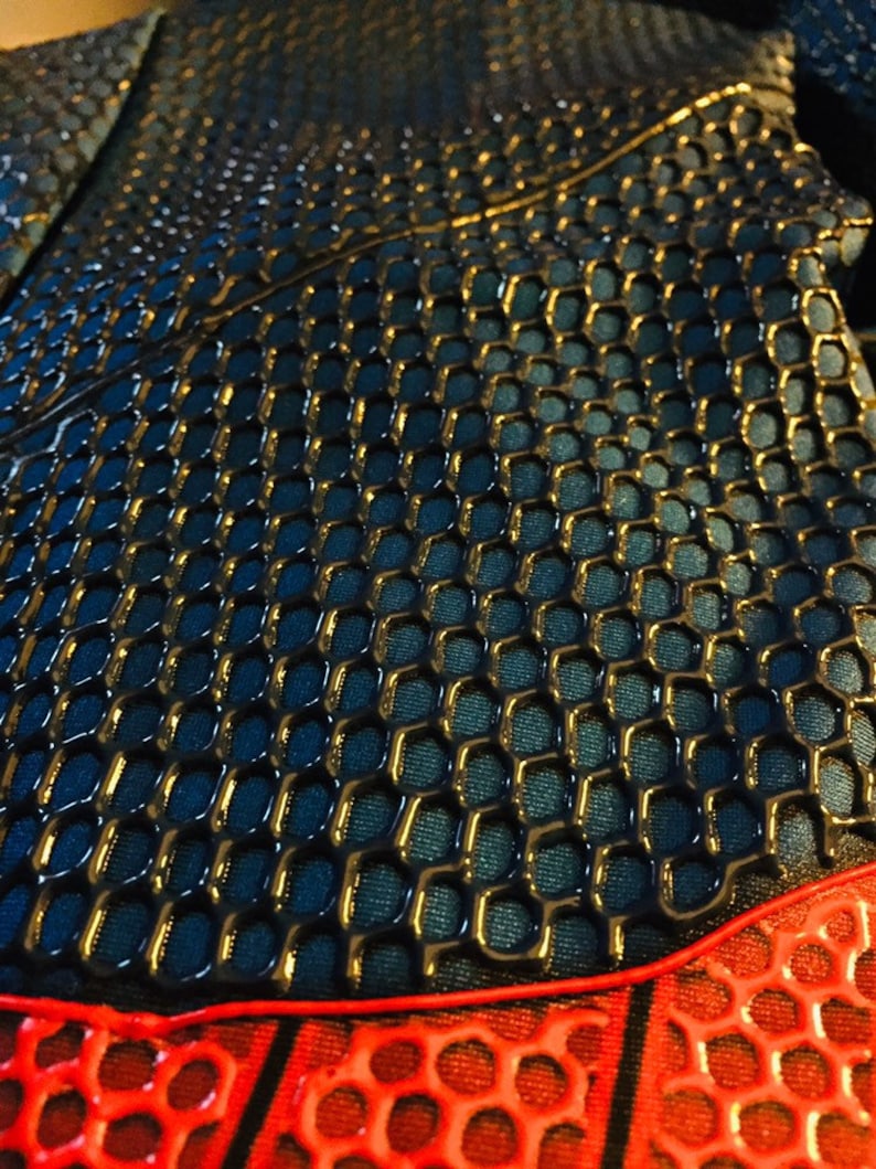 May include: Close-up of a black and red fabric with a honeycomb pattern. The fabric has a shiny, almost wet look.