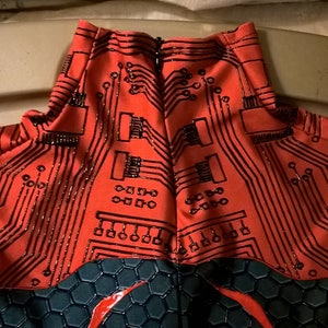 May include: Red and black bodysuit with a circuit board pattern. The back of the bodysuit has a zipper.