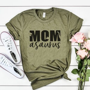 May include: A green t-shirt with the text "MOMasaurus" in black lettering. The text includes a dinosaur silhouette in the "O" of MOM.