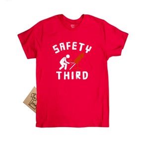 K&ouml;nnte beinhalten: Ein leuchtend rotes T-Shirt mit dem wei&szlig;en Schriftzug "SAFETY THIRD", zusammen mit einer Strichm&auml;nnchen-Figur und einer Rakete. Ein kleines Etikett ist angebracht. Es ist ein Freizeitkleidungsst&uuml;ck.