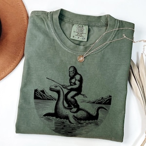 Bigfoot Riding Loch Ness Monster screen printed T-Shirt, Funny Cryptid Graphic Tee, Unisex Casual T-Shirt, Gift for Him, Comfort Colors