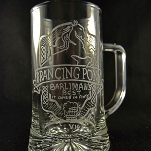 May include: Clear glass beer mug with a handle, featuring etched artwork and text. The design includes a prancing horse, Celtic knotwork, and the words "PRANCING PONY" and "BARLIMAN'S BEST IT COMES IN PINTS". The mug has a decorative base.