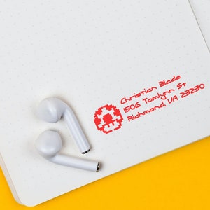 Custom return address stamp on a dotted notebook page with earbuds, showcasing a creative address stamp design. Perfect for personalized mail, this custom rubber stamp adds a unique touch to your correspondence. Ideal for creative and practical use.