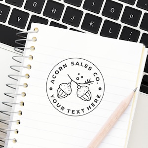 Create your own stamp with this large custom stamp featuring a customized logo stamp design. Perfect for personalizing stationery, the stamp is shown on a notebook beside a keyboard and pencil, highlighting its use for branding and creativity.