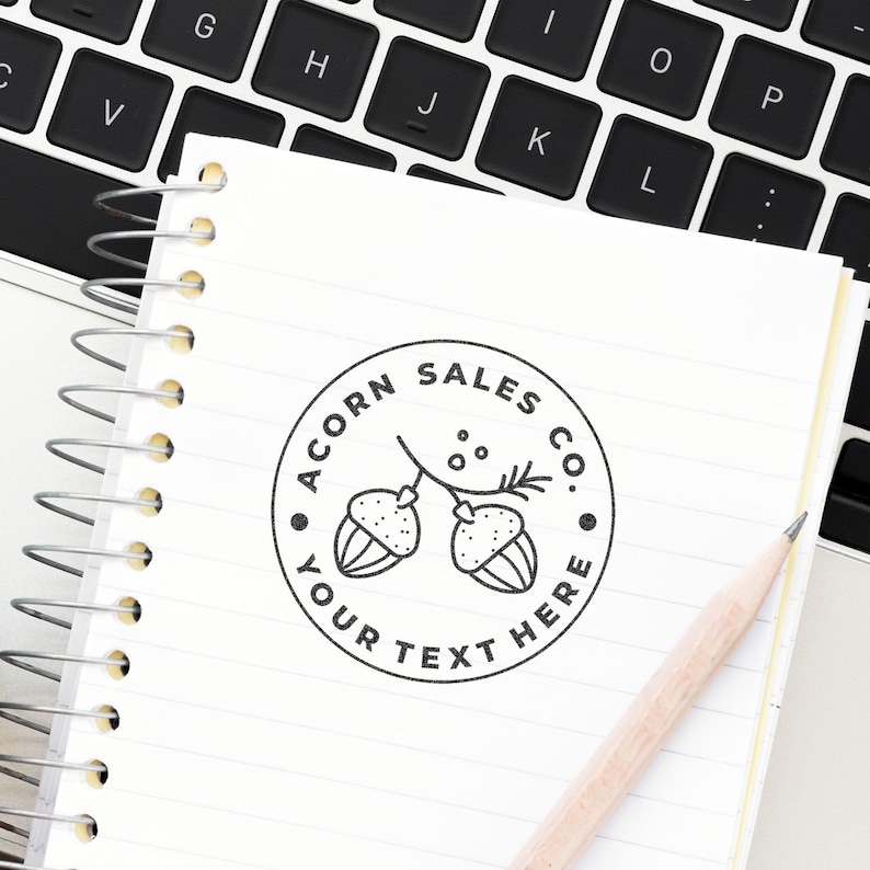 Create your own stamp with this large custom stamp featuring a customized logo stamp design. Perfect for personalizing stationery, the stamp is shown on a notebook beside a keyboard and pencil, highlighting its use for branding and creativity.