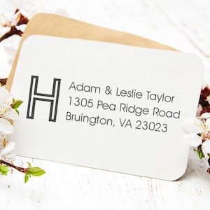 May include: A white return address label with a black letter "H" in a bold, sans-serif font. The text "Adam & Leslie Taylor 1305 Pea Ridge Road Bruington, VA 23023" is printed in black below the letter.