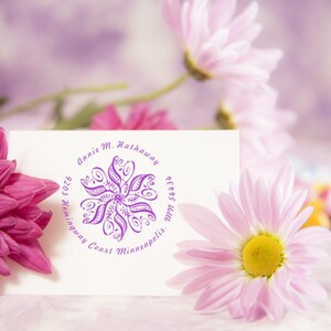 Custom rubber stamp featuring a floral design and personalized text, ideal as an address stamp for gifts. This custom self-inking address stamp adds a personal touch to any correspondence, surrounded by pink and white flowers.