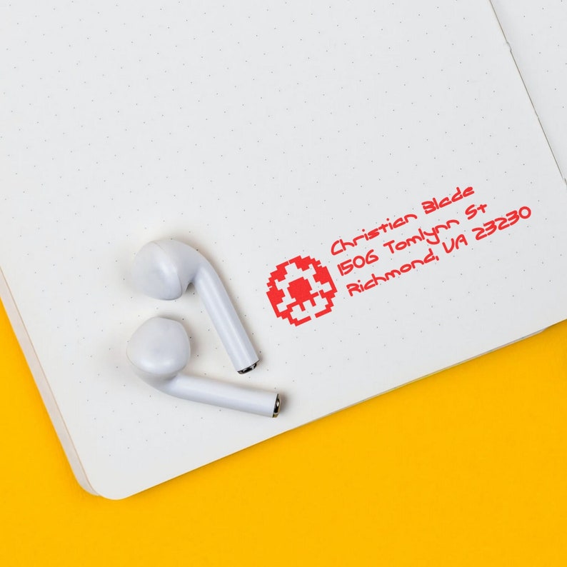 Custom return address stamp on a dotted notebook page with earbuds, showcasing a creative address stamp design. Perfect for personalized mail, this custom rubber stamp adds a unique touch to your correspondence. Ideal for creative and practical use.