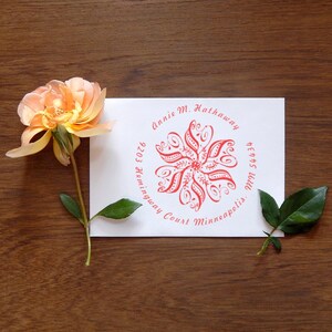 A self-inking address stamp featuring a floral design is displayed on an envelope, accompanied by a flower rubber stamp. The intricate pattern adds elegance to personalized correspondence.