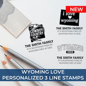 K&ouml;nnte beinhalten: Eine Sammlung personalisierter Stempel mit dem Text "Wyoming Love" und "Personalisierte 3-Zeilen-Stempel". Die Stempel zeigen verschiedene Designs, darunter "Cowboy Country" und "i love wyoming". Bleistifte sind im Vordergrund.