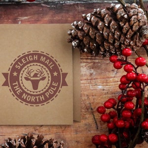 Unique Sleigh Mail Stamp on a rustic envelope, surrounded by festive pinecones and berries. Perfect for holiday stamping supplies. This self-inking stamp adds a charming touch to your seasonal correspondence.