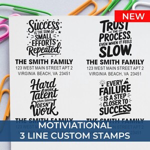 Four sample custom address stamp designs with motivational quotes and “The Smith Family” address, displayed on paper with colorful paper clips; text reads “Motivational 3 Line Custom Stamps” with a red “NEW” label.