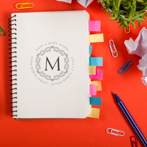 Personalized stamp on a notebook surrounded by colorful paper clips and a pen, ideal for home office supplies. Custom design adds a unique touch to your workspace essentials.