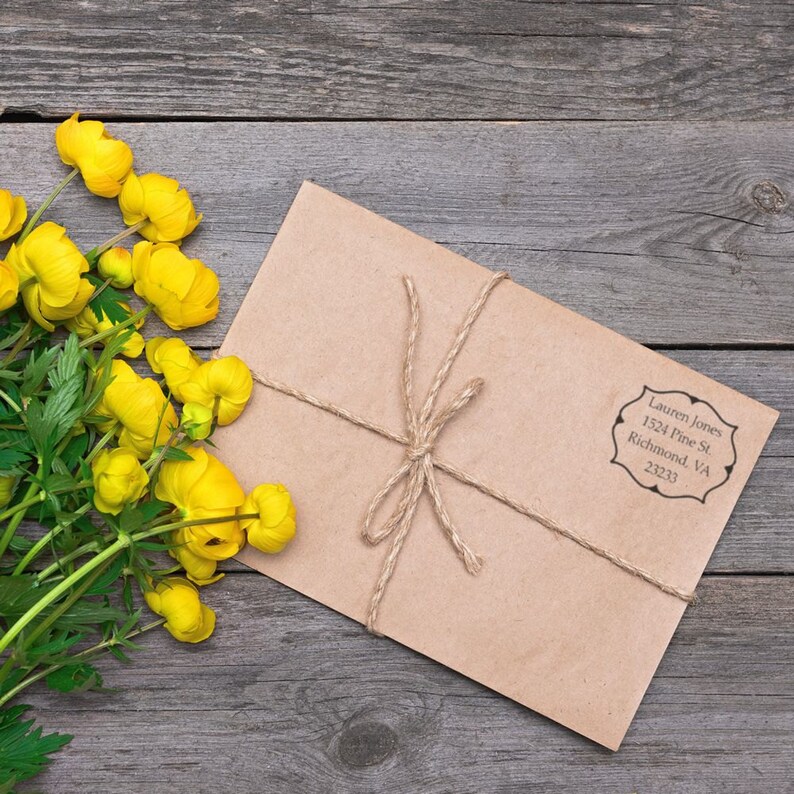 Envelope with a personalized address stamp beside yellow flowers on a wooden table. Ideal self-inking address stamp for personalized real estate gifts, adding a unique touch to correspondence.