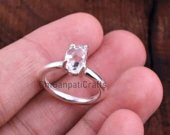 May include: A silver ring with a clear, faceted gemstone. The ring is set on a finger.