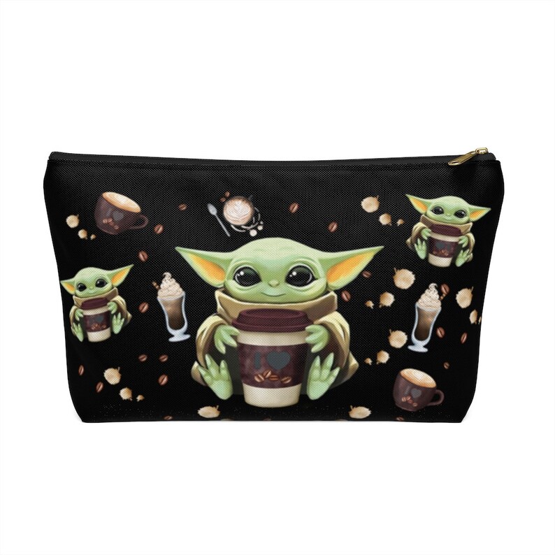 Puede incluir: Una bolsa de maquillaje de lona negra con un patr&oacute;n repetido de un personaje alien&iacute;gena verde sosteniendo una taza de caf&eacute;, granos de caf&eacute; y otras im&aacute;genes con tem&aacute;tica de caf&eacute;.