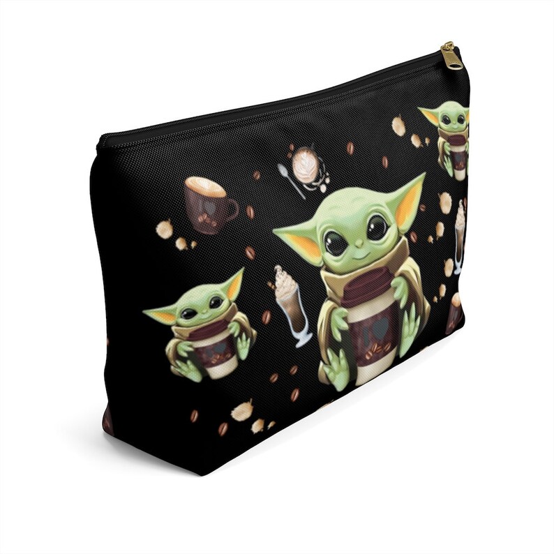 Puede incluir: Bolsa de maquillaje negra con cremallera con un patr&oacute;n repetido de un personaje alien&iacute;gena verde sosteniendo una taza de caf&eacute;, granos de caf&eacute; y una taza de caf&eacute; sobre un fondo negro.