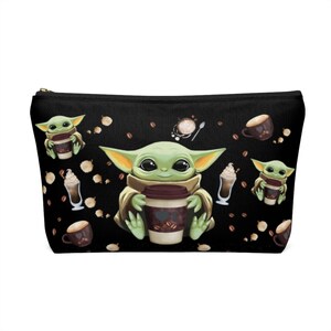 Puede incluir: Bolsa negra con cremallera con un patr&oacute;n repetido de un personaje alien&iacute;gena verde sosteniendo una taza de caf&eacute;, granos de caf&eacute; y tazas de caf&eacute;.